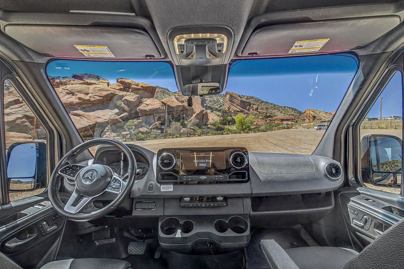 Interior of a Mercedes-Benz rv rental van, featuring the dashboard, steering wheel, infotainment screen, and a rugged outdoor view.