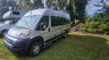 Ready for adventure! This silver Ram Promaster camper van RV rental sits on green grass, backed by trees, with another RV nearby.