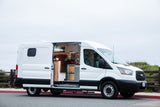 A bright white Ford Transit camper van, equipped for RV rental, showcases its cozy, custom interior through an open side door.