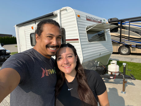 Happy couple by their Starcraft AR-ONE travel trailer, possibly an RV rental, with a large motorhome nearby.