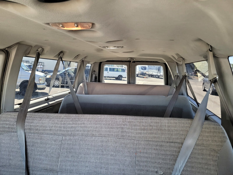 Interior of a passenger van, showing rows of grey fabric seats and hanging seatbelts. An RV rental and other vehicles are visible outside. — photo 5