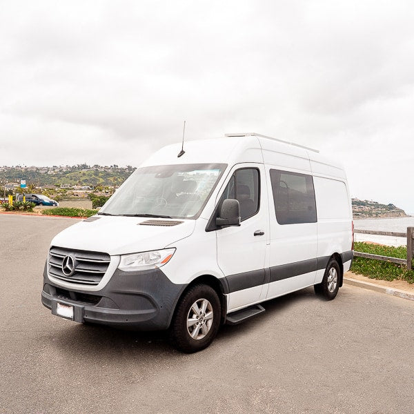  and a yellow-cushioned bench visible via the open door.|Open back of an RV rental: a person relaxes inside a custom camper van with a cozy bed — photo 2