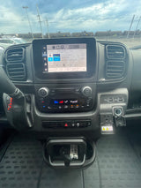 Inside an RV rental, showing the modern dashboard with infotainment playing music, climate controls, and a view of train cars outside.