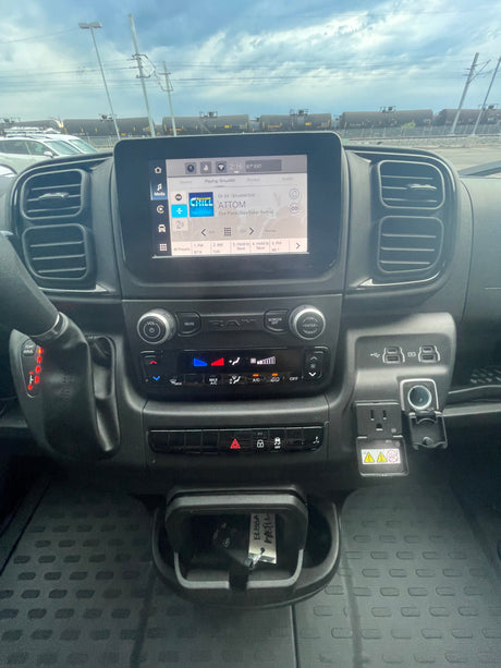 Inside an RV rental, showing the modern dashboard with infotainment playing music, climate controls, and a view of train cars outside.