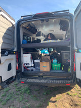 Inside an **RV rental**, a person rests on the top bunk of a camper van. Below, organized storage & portable shower for van life.
