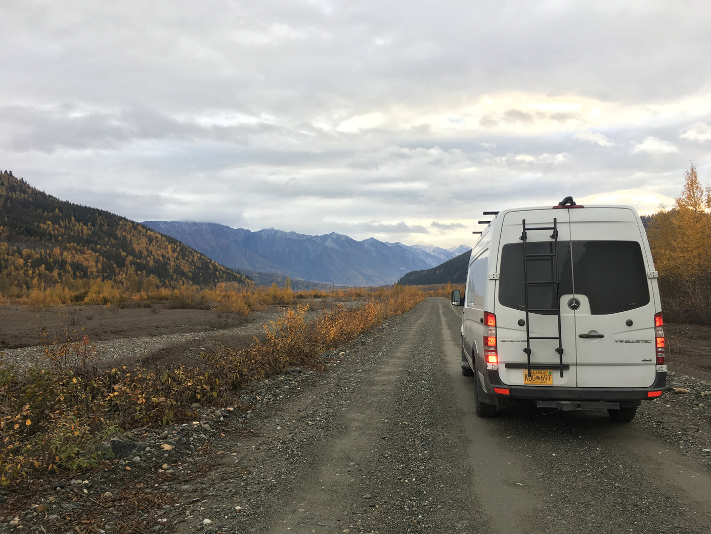 Adventurous rv rental: a white Sprinter van on a gravel road in Alaska's autumn mountains.