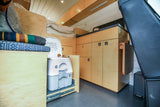 RV rental: compact interior with light wood cabinetry, a pull-out portable toilet, and an elevated sleeping bunk.