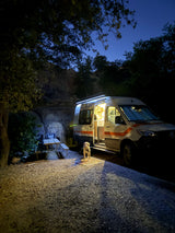 Nighttime RV rental: A dog waits by the glowing camper at a scenic site, while someone prepares food inside.