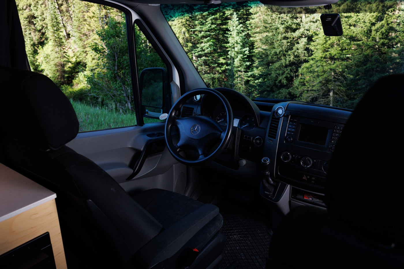 Mercedes-Benz Sprinter camper van RV rental cockpit view: dashboard, steering wheel, driver's seat, forest outside. — photo 13