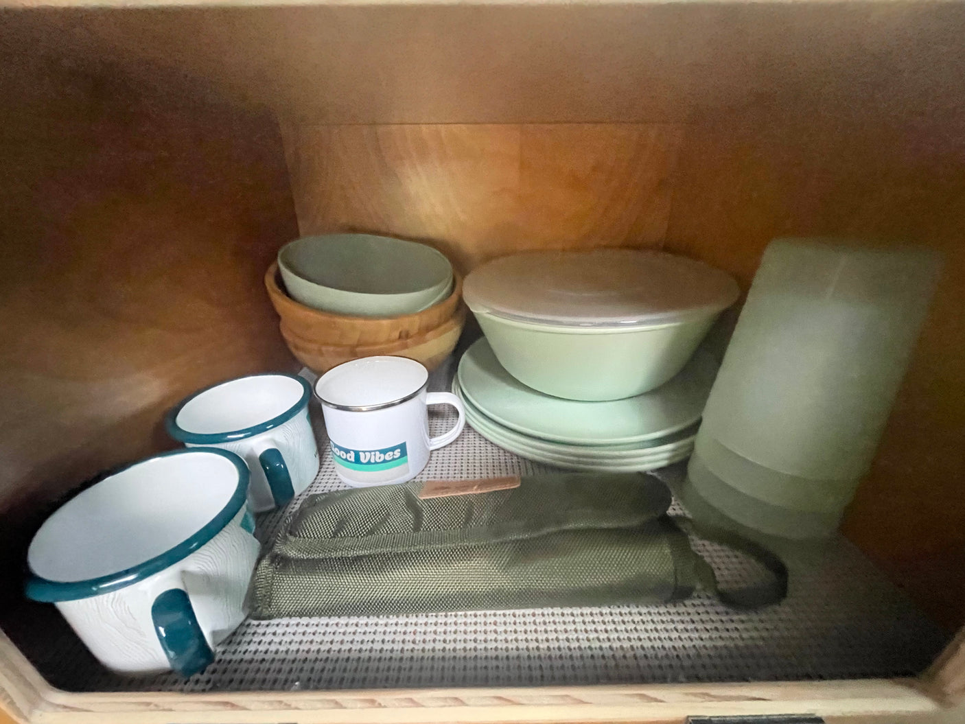 RV rental kitchen supplies: organized light green plates, bowls, enamel mugs, wooden bowls, and a green fabric pouch.
