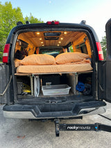 Back of a custom-built RV rental camper van, showing a cozy bed, wood ceiling, and under-bed storage.