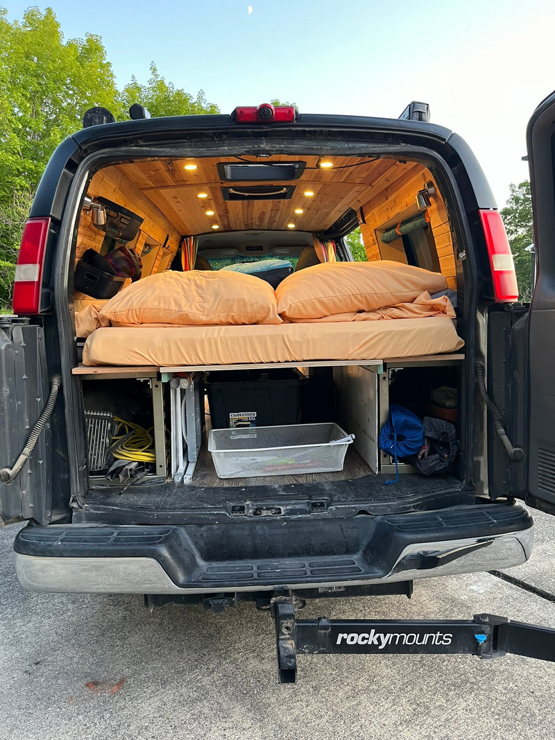Back of a custom-built RV rental camper van, showing a cozy bed, wood ceiling, and under-bed storage. — photo 15
