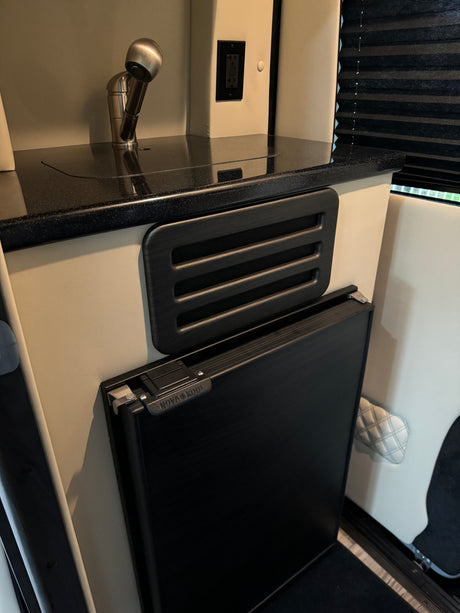 An RV rental's compact kitchen features a shiny faucet, speckled counter, air vent, and a Nova Kool refrigerator.