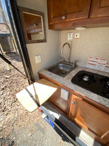 Compact RV rental kitchen with sink, stove, cabinets, and a convenient fold-out table for outdoor cooking access.