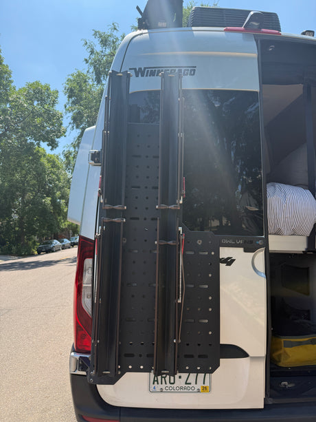 Rear of a Winnebago camper van with a cargo rack and partially open door, ideal for an rv rental adventure. Plate ARU-Z77.