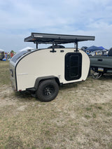 Teardrop RV rental: a compact, white trailer with a Kammok awning attached to a pickup truck, ideal for camping.