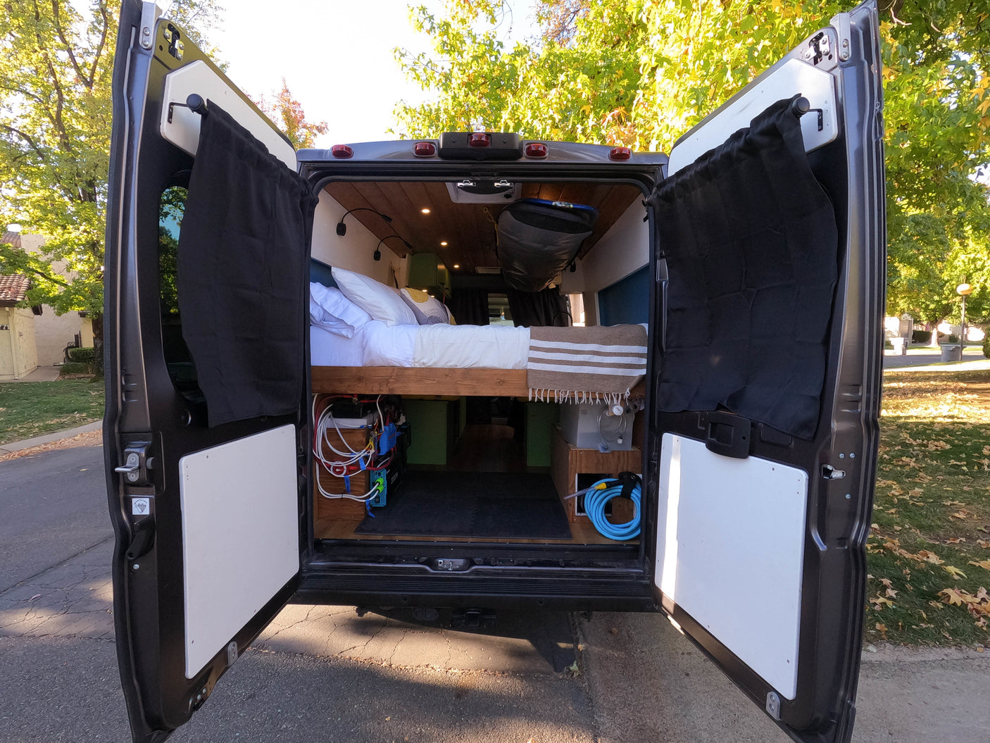 Explore this cozy RV rental's interior. The open rear of this custom camper van reveals a comfortable bed, storage, and power setup.