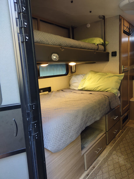 Inside a comfortable rv rental: two bunk beds with quilted blankets, bright pillows, and convenient under-bed storage drawers.