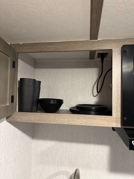 RV rental kitchen cabinet with black plates, bowls, and cups, plus an outlet and cord for appliances.