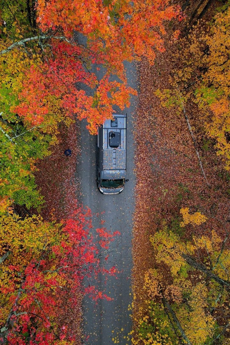 Overhead view of an RV rental on a road, flanked by vivid red, orange & yellow autumn leaves.