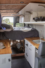 RV rental interior: cozy bed, full kitchen w/ sink, wooden counters, overhead projector, and under-bed storage.