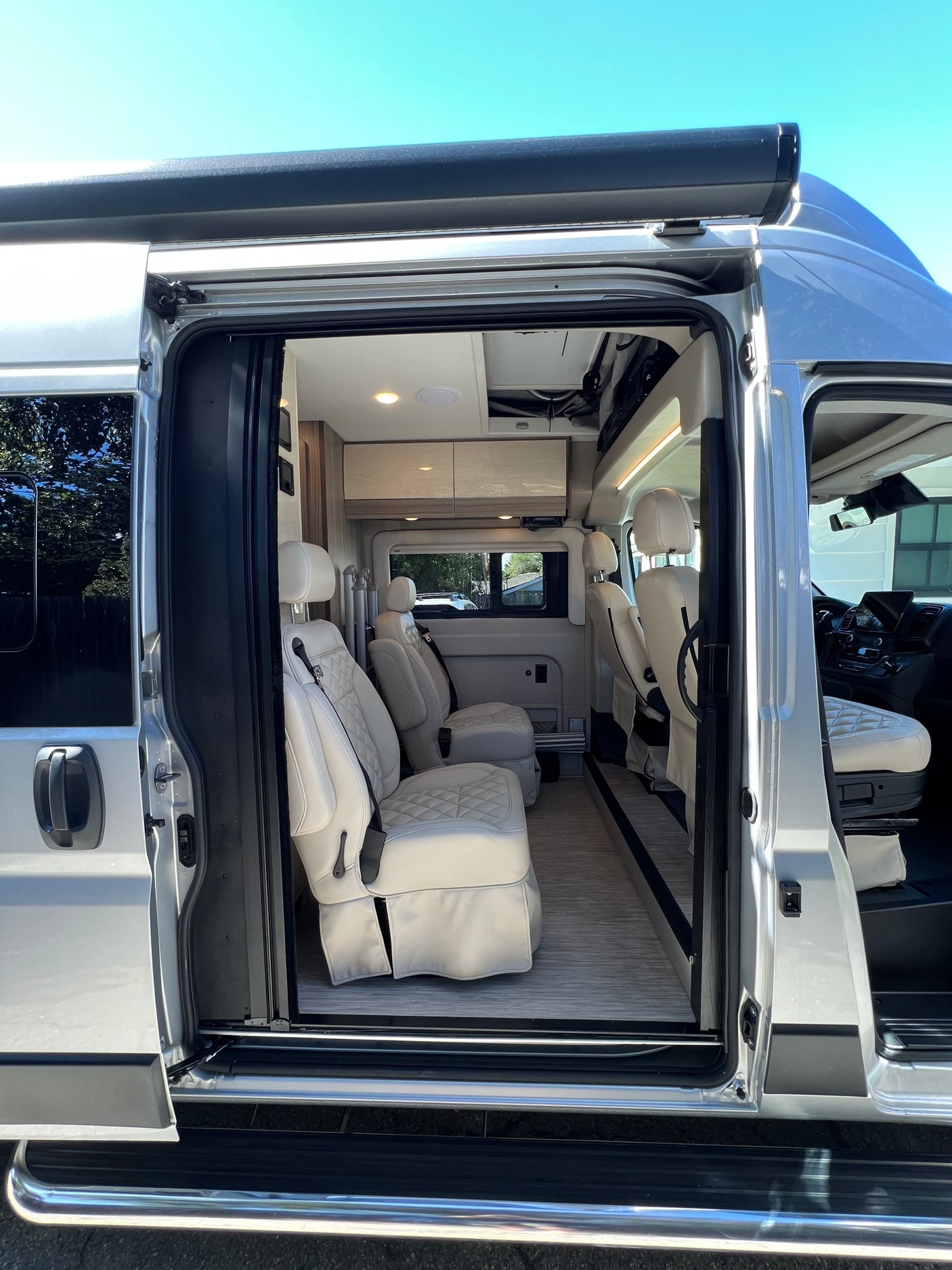 This RV rental camper van offers a luxury interior. See the spacious cabin with white quilted seating from the open sliding door.