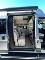 This RV rental camper van offers a luxury interior. See the spacious cabin with white quilted seating from the open sliding door.
