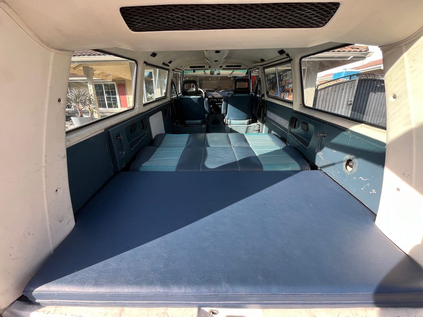 An RV rental van's interior, viewed from the rear. Blue seats are folded flat, forming a bed; front cabin and windows are visible. — photo 4