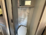 Compact RV rental bathroom featuring a white toilet, wall-mounted shower head, and small mirror above.