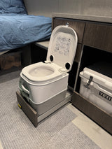 Portable cassette toilet on a pull-out tray in a compact RV rental interior, next to a bed and Yeti cooler.
