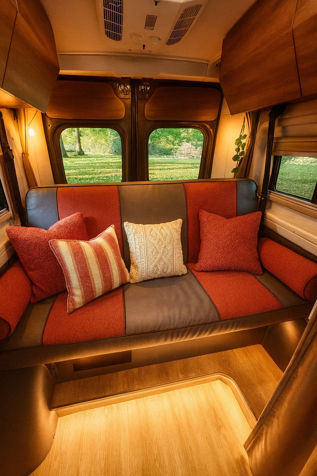 Cozy RV rental interior featuring a two-toned sofa with various pillows, warm ambient lighting, and a serene nature view.