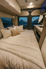 Cozy RV rental bedroom with a plush bed, textured blanket, and serene mountain lake views from the windows for a peaceful night.
