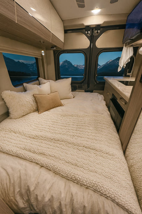 Cozy RV rental bedroom with a plush bed, textured blanket, and serene mountain lake views from the windows for a peaceful night.