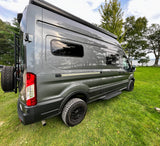 Ready for adventure! This grey camper van, perfect for your next rv rental, is parked on lush grass by a lake.