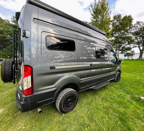 Ready for adventure! This grey camper van, perfect for your next rv rental, is parked on lush grass by a lake.
