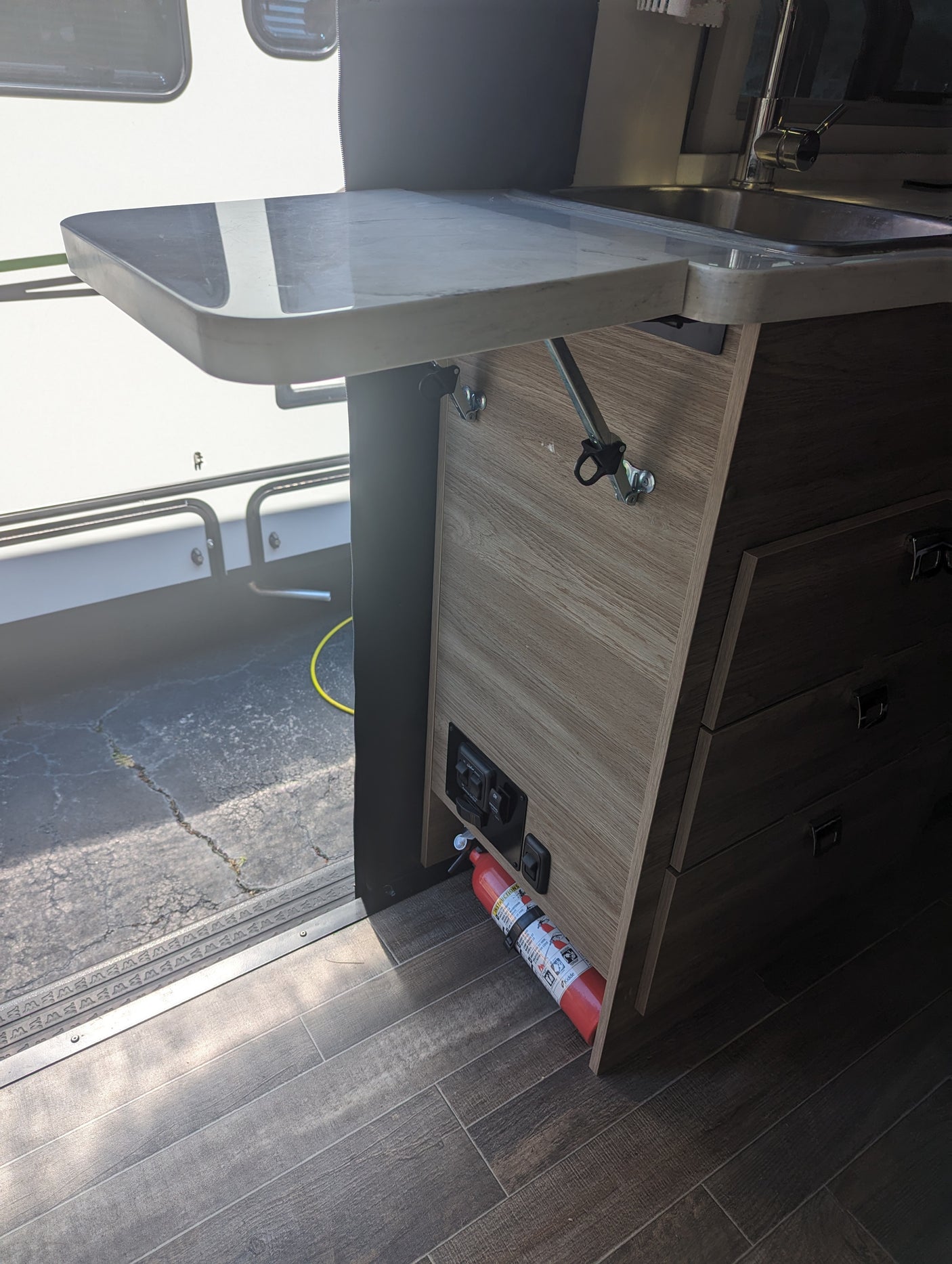 Inside an RV rental: Compact kitchen with a sink, extendable counter, and a fire extinguisher for safety.