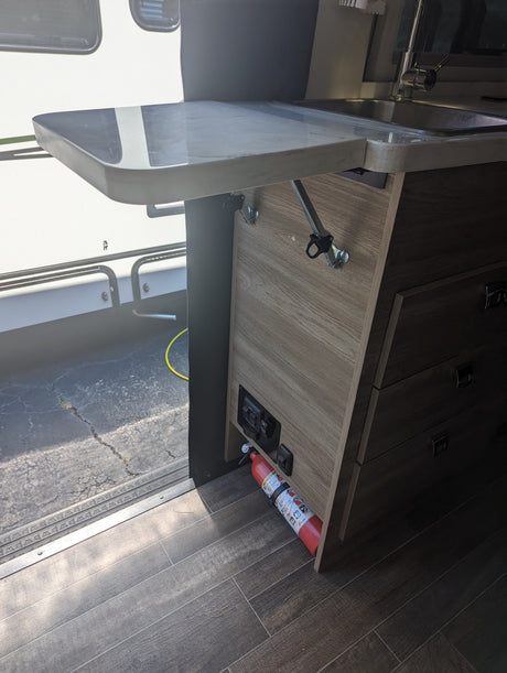 Inside an RV rental: Compact kitchen with a sink, extendable counter, and a fire extinguisher for safety.