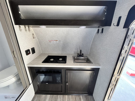 Functional RV rental interior: a compact kitchen with stove, sink, microwave, and adjacent toilet for camper convenience.