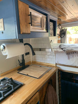 Compact RV rental interior featuring a functional kitchen with stove, sink, microwave, and a cozy bed area.