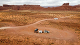 Overhead view of desert camping. An RV rental is on a dirt road, while cars & a teardrop trailer are parked below.