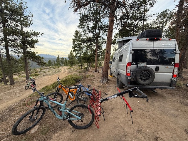  parked in a scenic forest setting overlooking mountains.|RV rental camper van parked in a forest campsite with a bike rack & dog relaxing nearby. Pop-top up.|RV rental: Camper van & mountain bikes on a scenic dirt trail — photo 4