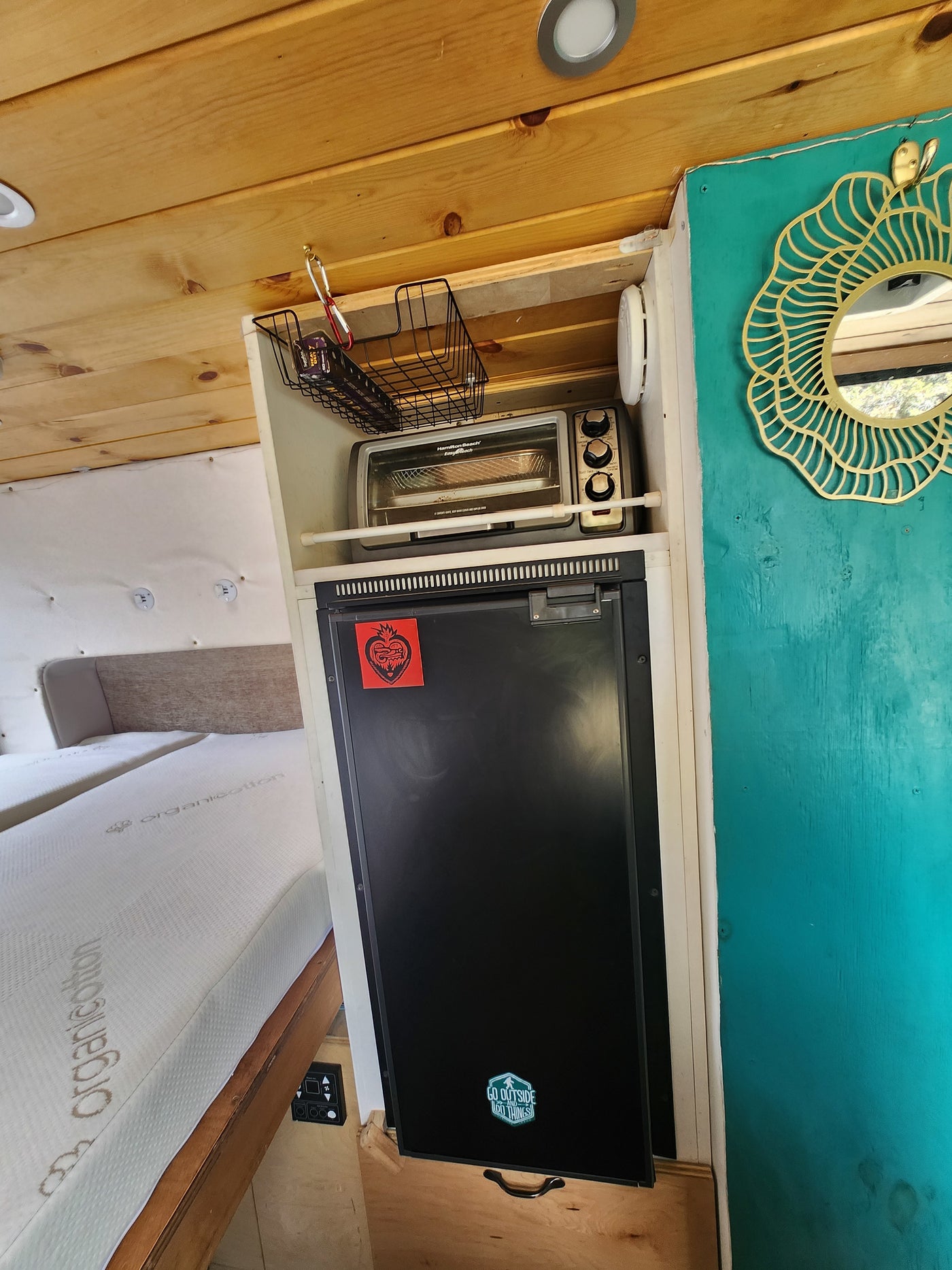 Inside an RV rental: a compact kitchen with toaster oven & fridge, plus a cozy bed, designed for travel comfort. — photo 8