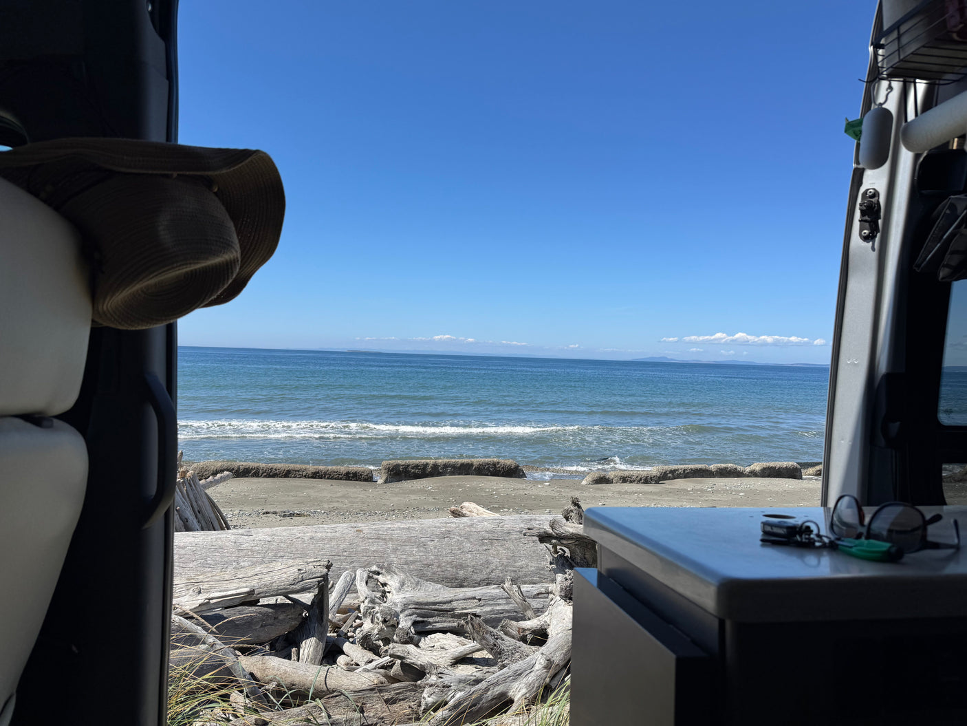 Ocean and driftwood view from an RV rental. Enjoy seaside van life with keys & hat visible inside, gazing at the sea.