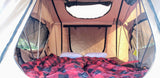 Cozy interior of an RV rental rooftop tent. Features a comfortable bed with red and black plaid bedding, metal poles, and mesh windows.