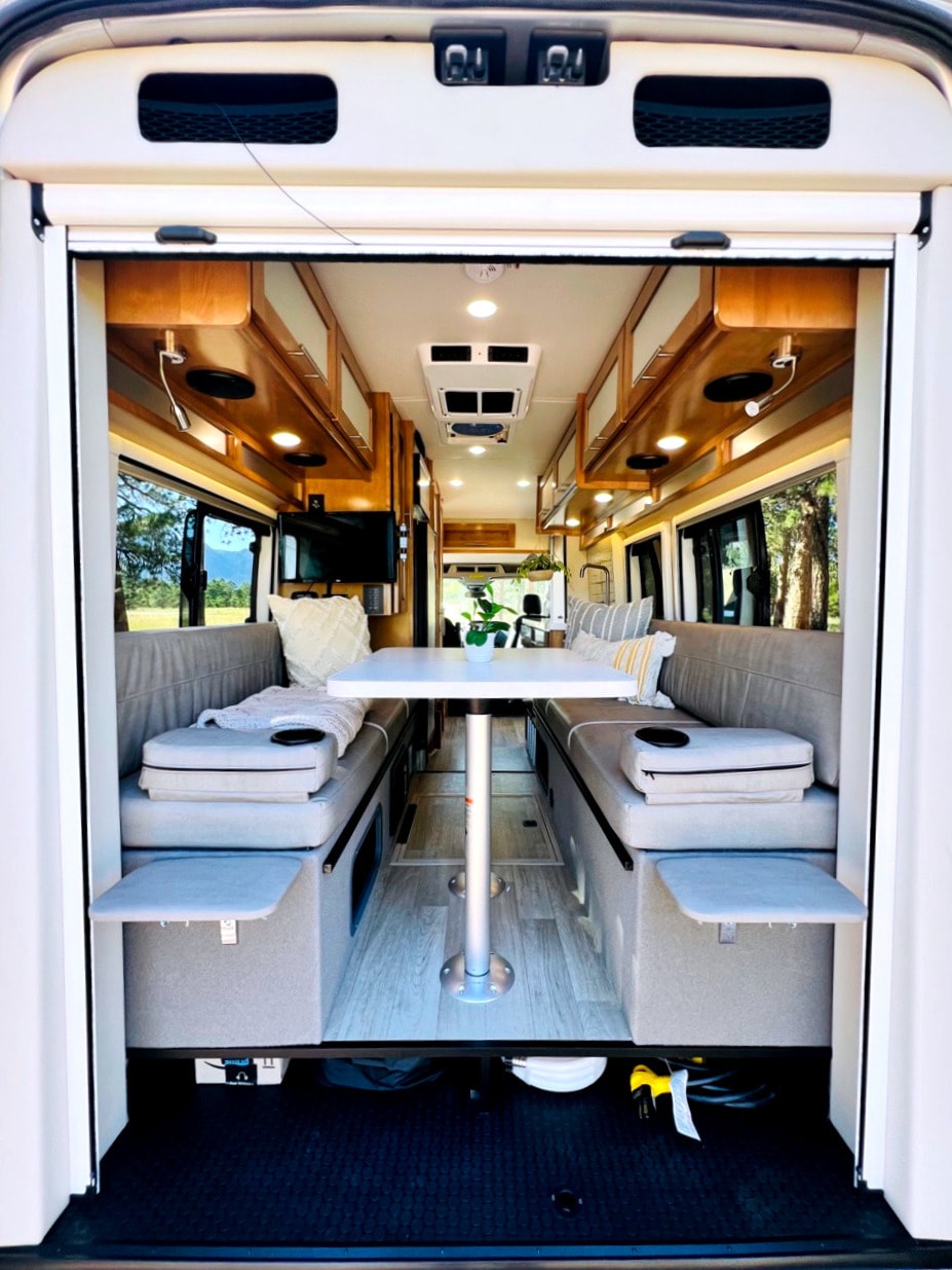This RV rental features a comfortable interior with twin bench seating, a central table, and overhead cabinets. — photo 13