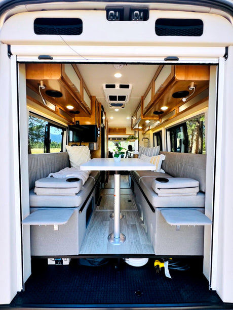 This RV rental features a comfortable interior with twin bench seating, a central table, and overhead cabinets.