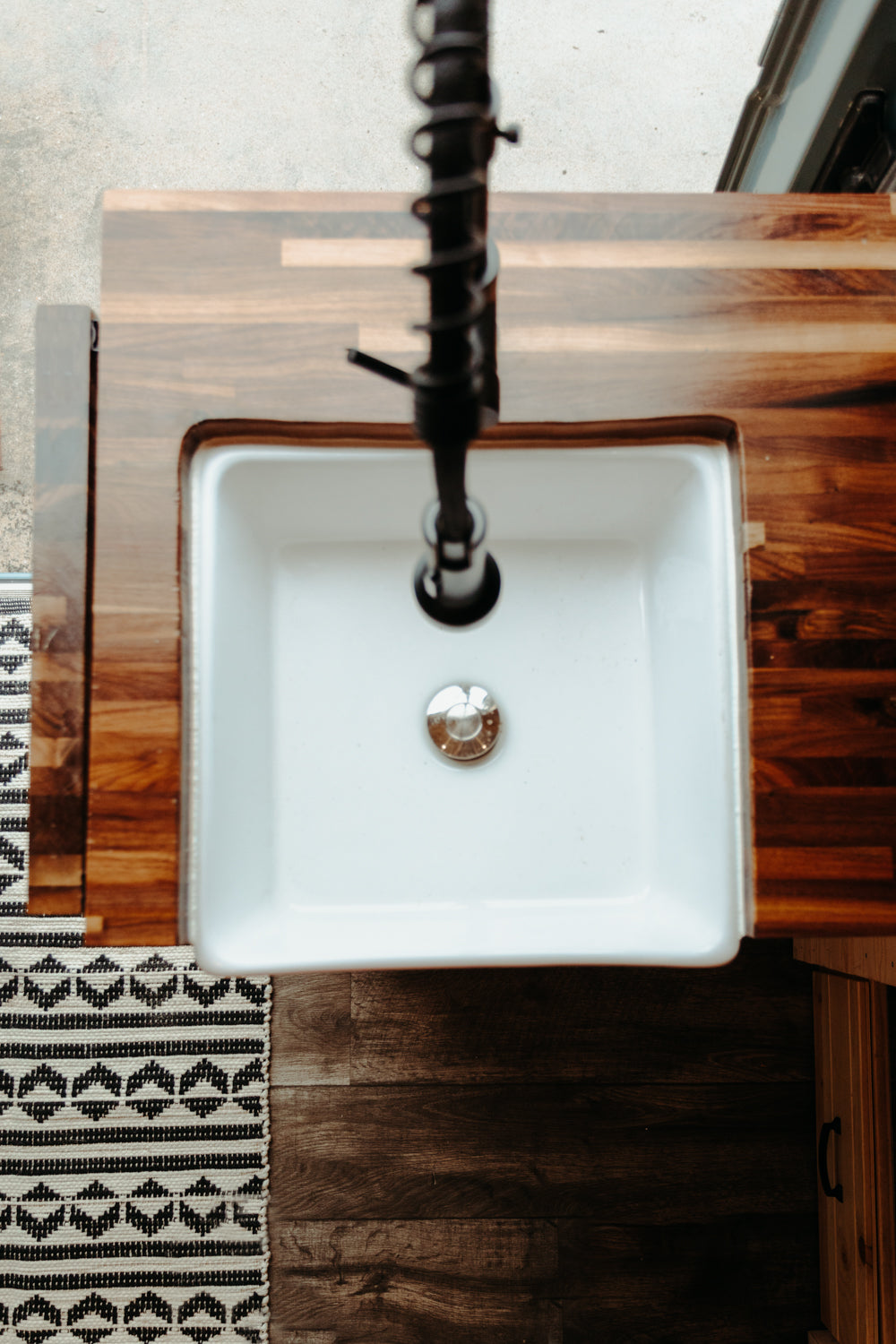 Overhead view of an RV rental kitchen: white sink, dark wood counter, and black pull-down faucet.