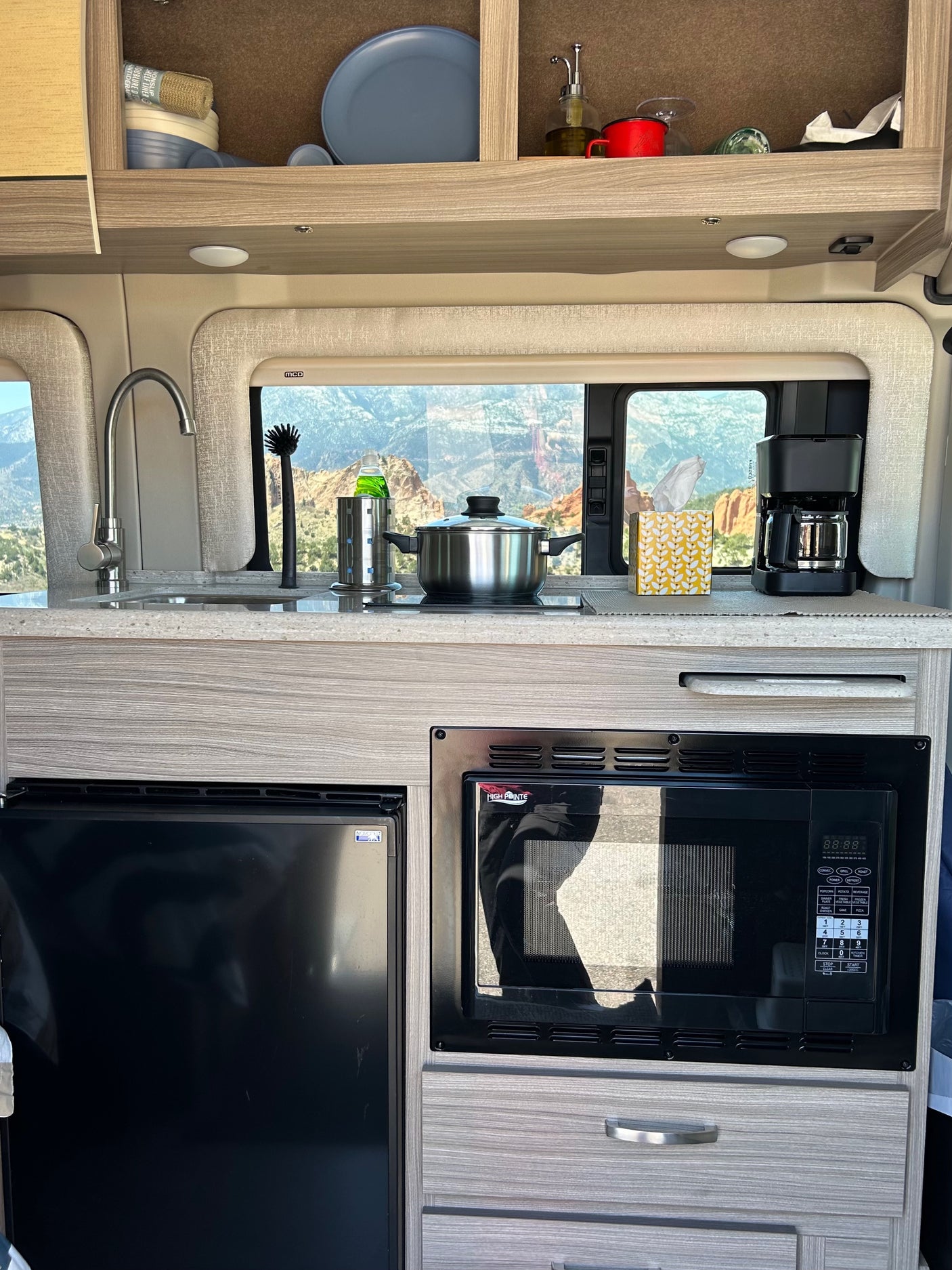 Modern RV rental kitchen featuring a sink, cooktop with pot, microwave, fridge, coffee maker, and scenic mountain view.
