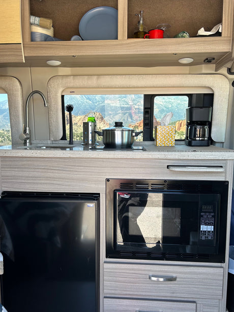 Modern RV rental kitchen featuring a sink, cooktop with pot, microwave, fridge, coffee maker, and scenic mountain view.