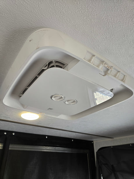 This RV rental's ceiling features a white air conditioner unit with visible control knobs, vents, and an adjacent light.
